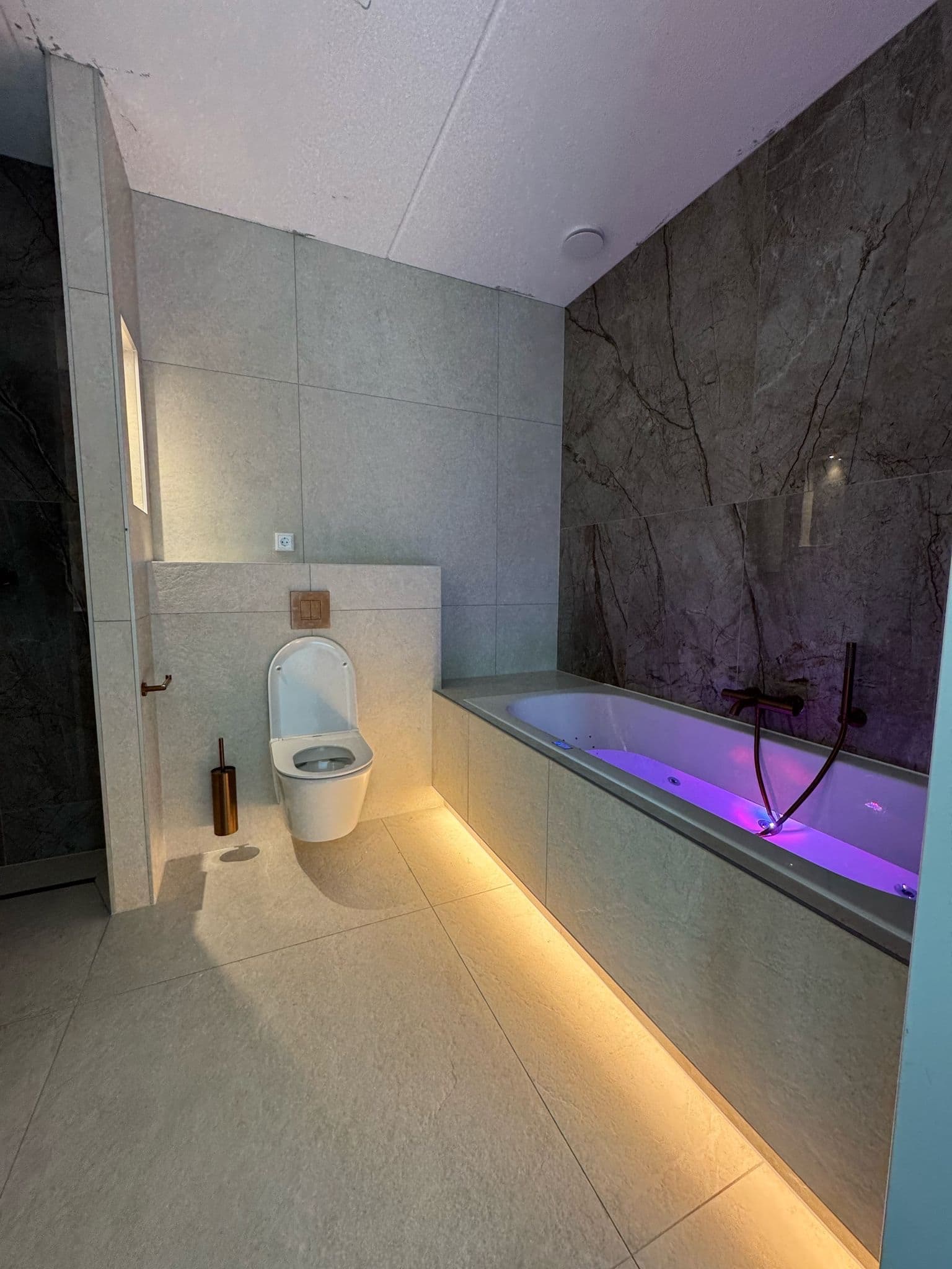 Ligbad en wandtoilet met warme indirecte verlichting