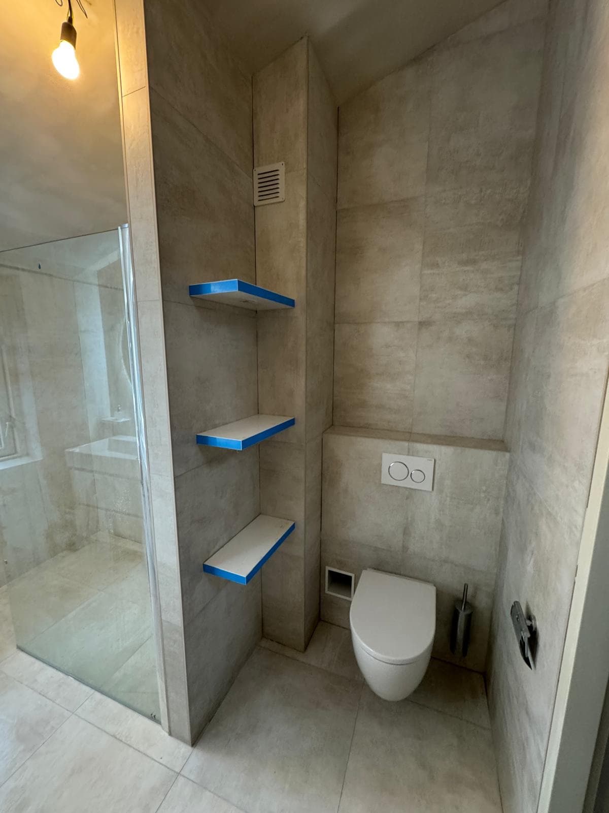 Wandtoilet met drie zwevende planken naast de glazen douche