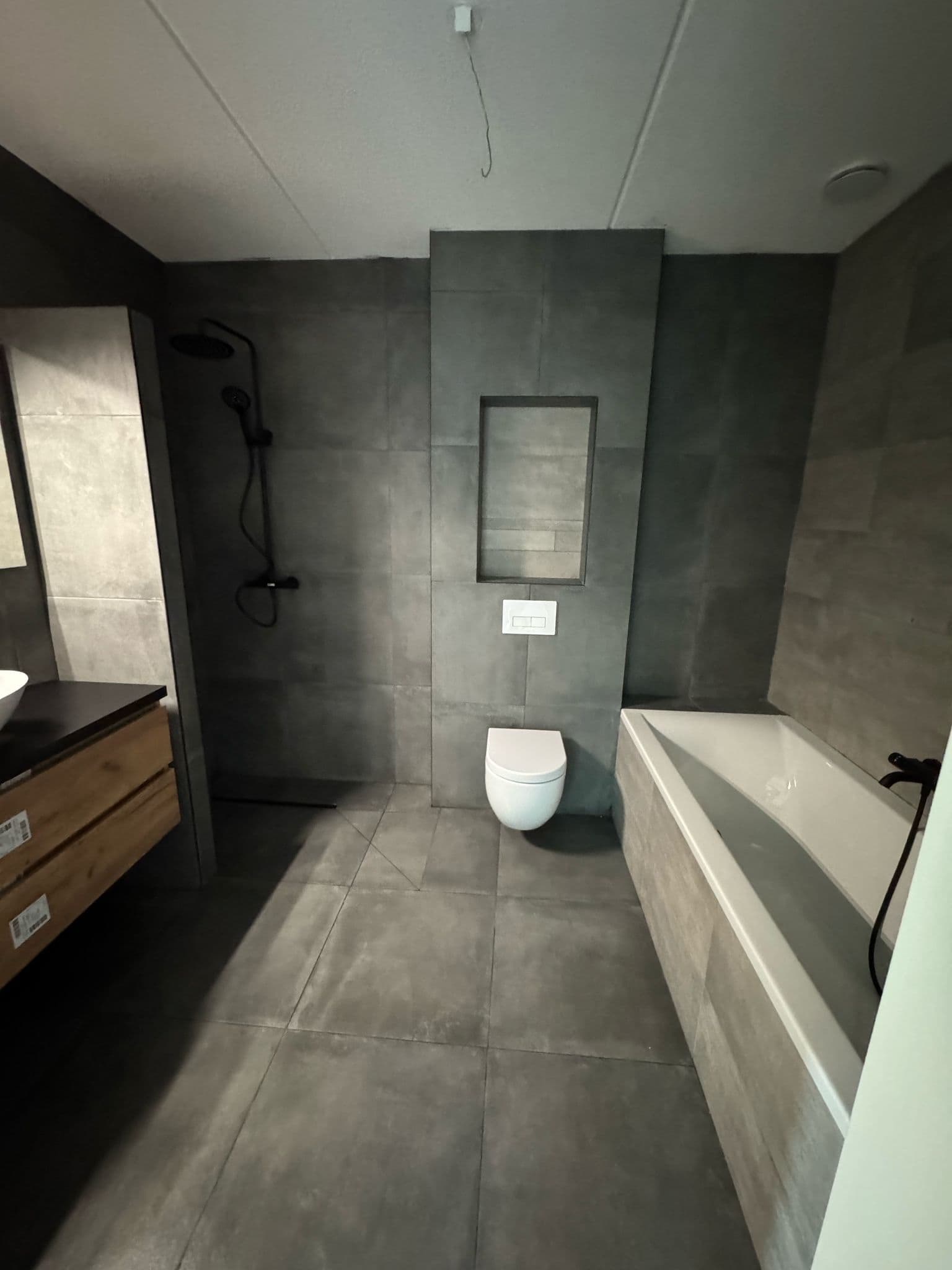 Badkamer met ligbad, wandtoilet en douche in donkergrijze tegels