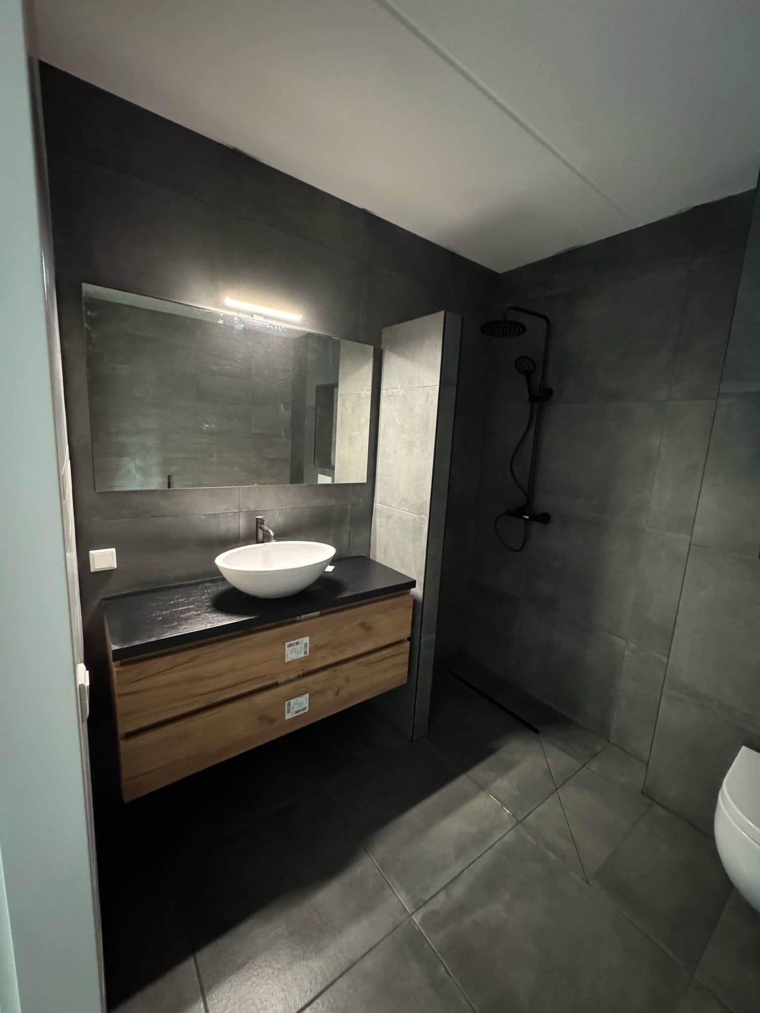 Donkergrijze badkamer met houtkleurig wastafelmeubel en open douche